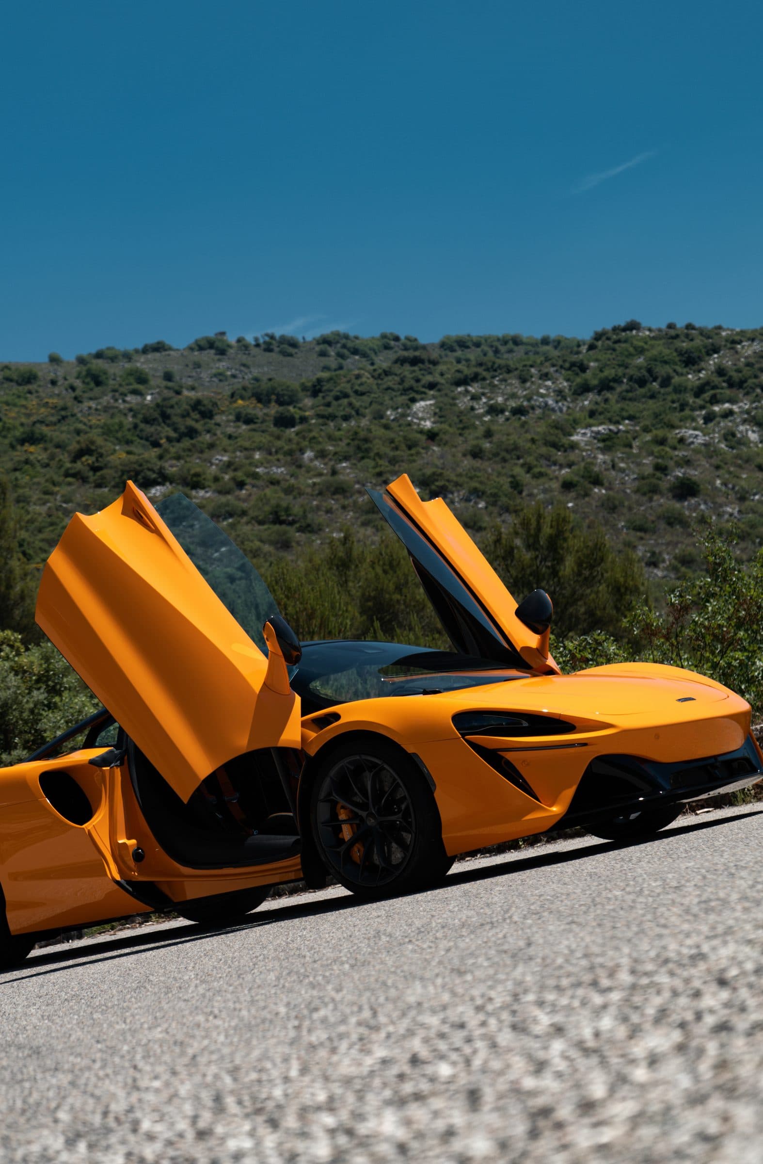 McLaren, portes papillon ouvertes, sur une route de montagne